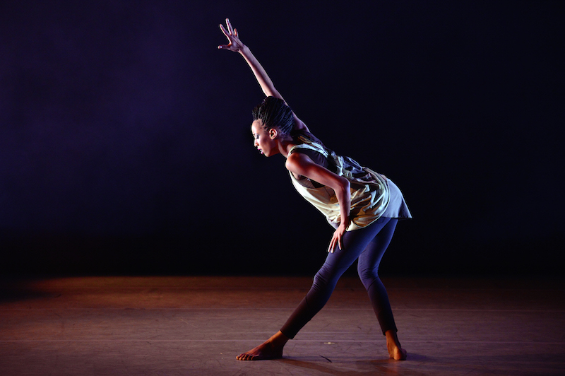 Courtney Celeste lunges. Her eyes are downcast. Her right arm extends on a diagonal above her head while her left rests on her thigh.